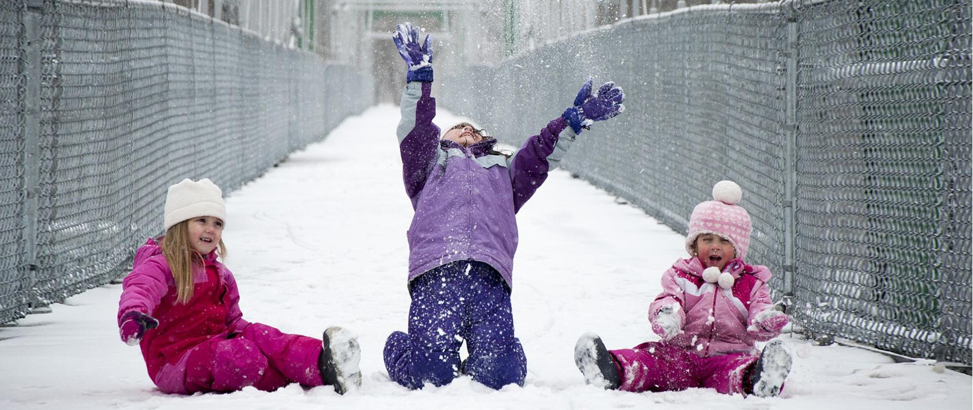 Troje dzieci w zimowych strojach bawią się na śniegu.