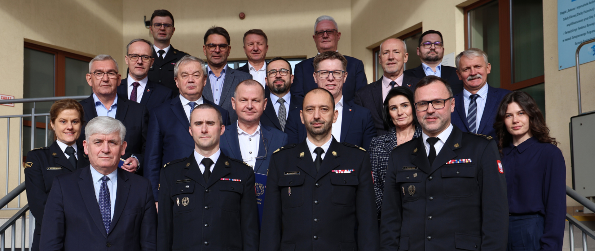 Grupa osób stoi na schodach przed wejściem do budynku 