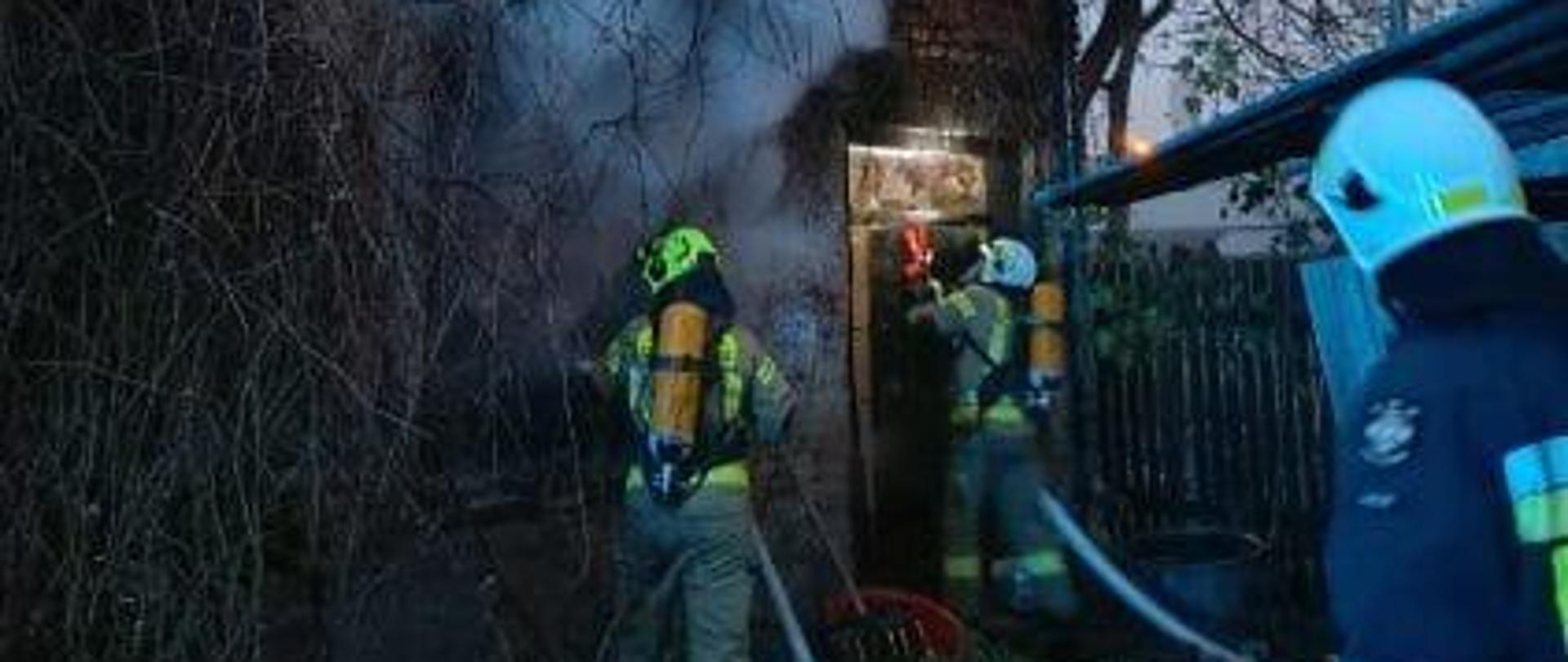Strażacy przed budynkiem objętym pożarem prowadza działania gaśnicze