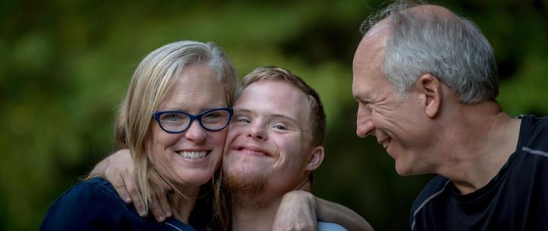 Rodzina. Matka przytula syna z zespołem Downa. Obok nich uśmiechnięty tata.