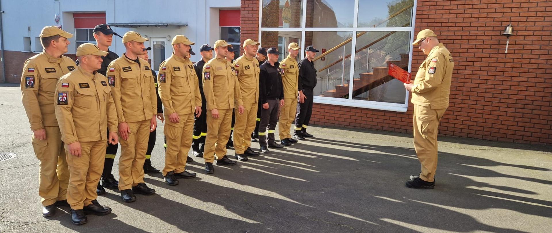 Strażacy stoją na placu komendy podczas przemowy komendanta.