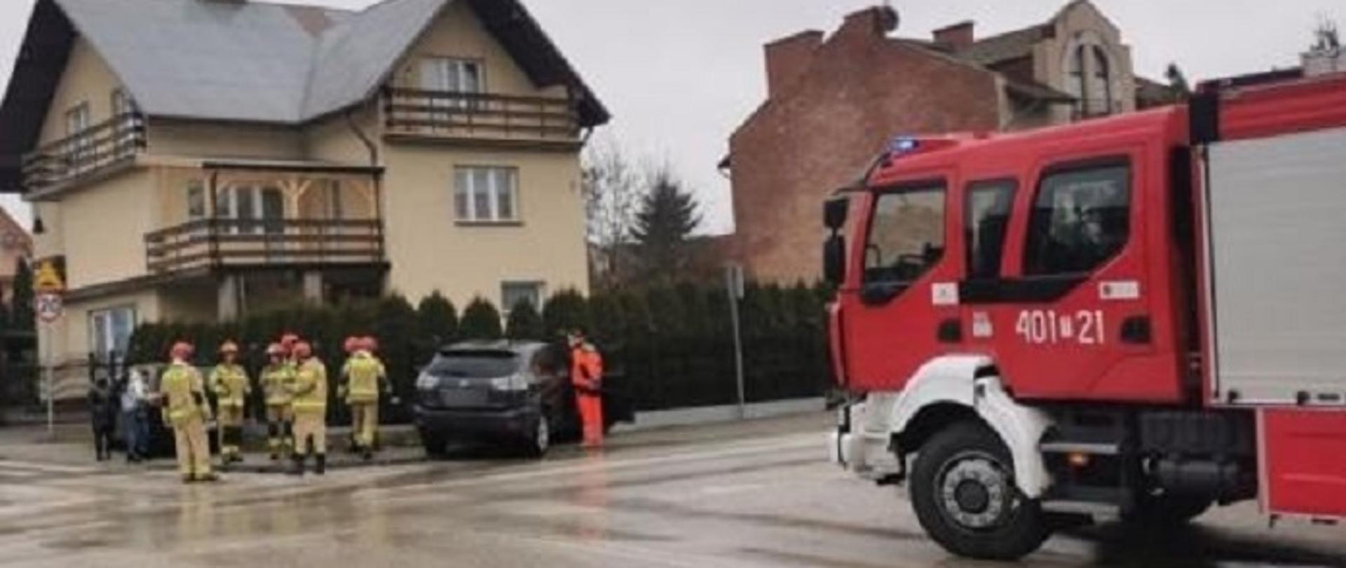 Zdjęcie przedstawia strażaków prowadzących działania ratownicze podczas wypadku drogowego w tle samochód pożarniczy