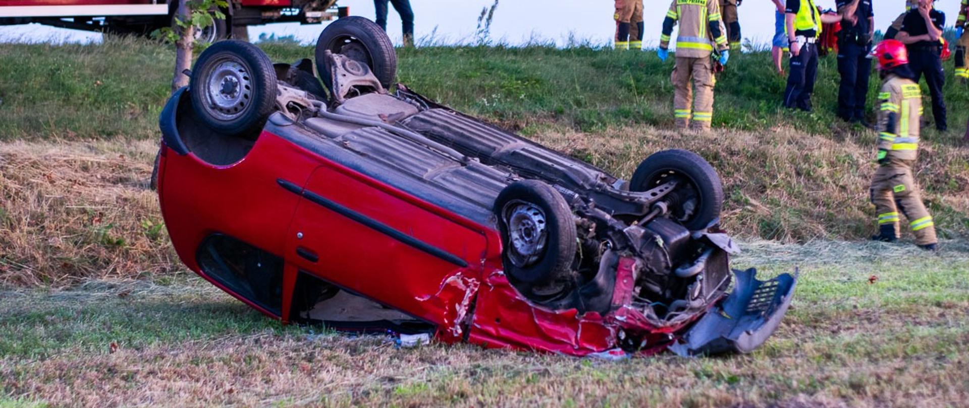 Na zdjęciu strażacy przy pojeździe znajdującym się na dachu.
