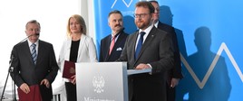 Minister zdrowia Łukasz Szumowski zapowiedział na konferencji prasowej ogólnonarodową debatę o kierunkach zmian w ochronie zdrowia. Zdjęcie na tle niebieskiej ścianki Ministerstwa Zdrowia wraz z członkami komitetu organizacyjnego debaty.