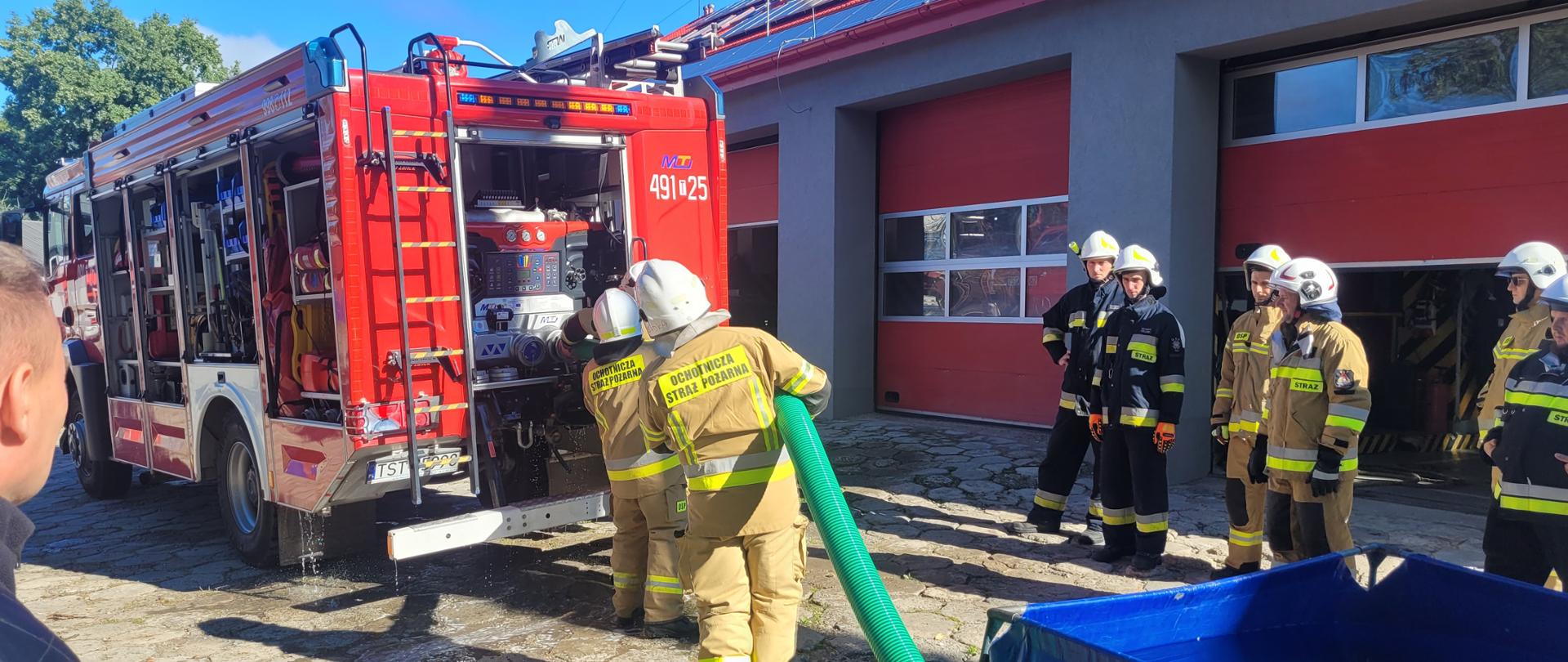 Strażacy obsługujący autopompę pożarniczą, z prawej strony zbiornik na wodę.