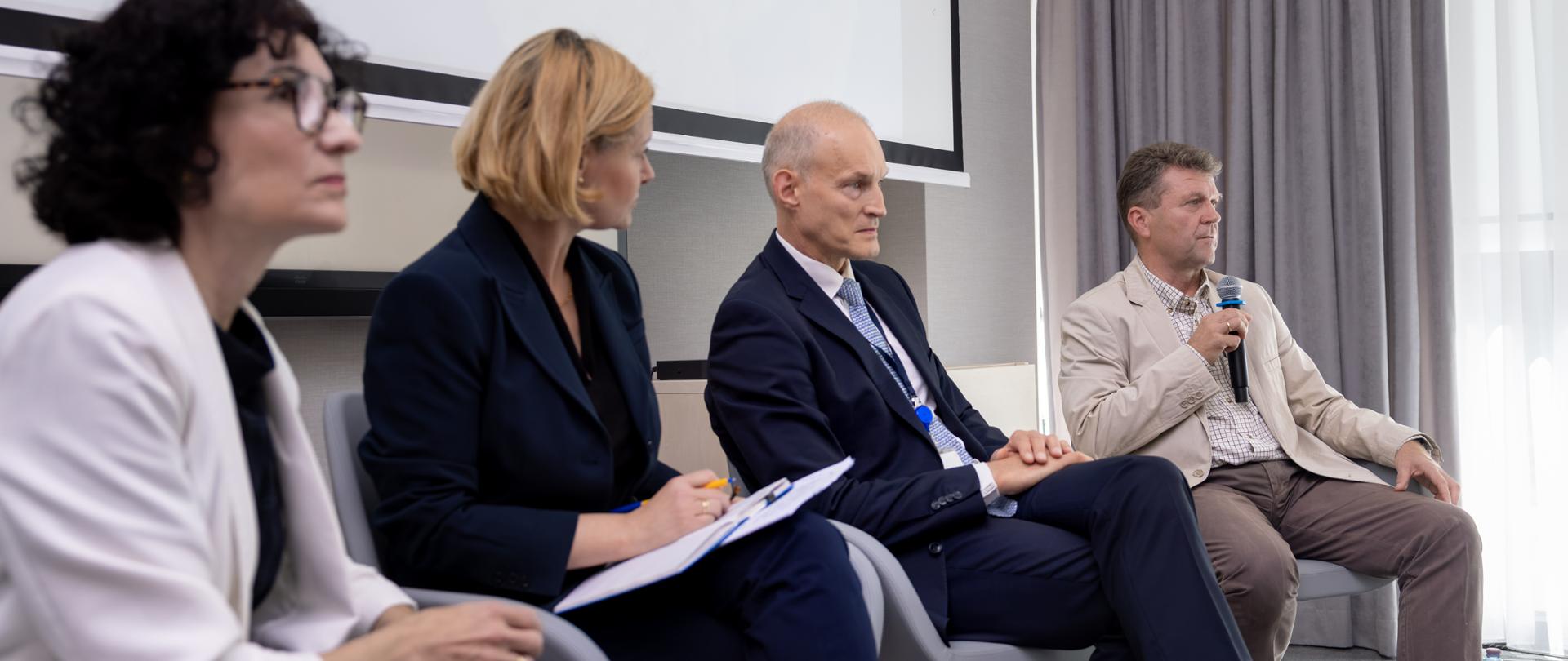 Four people are taking part in a panel discussion, seated in armchairs in the conference room. Deputy Minister Zajączkowski is sitting in the middle.