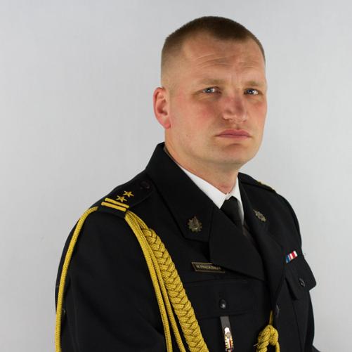 Mężczyzna w mundurze na białym tle, mundur czarny, po lewej stronie znajduje się sznur galowy zwisający od ramienia