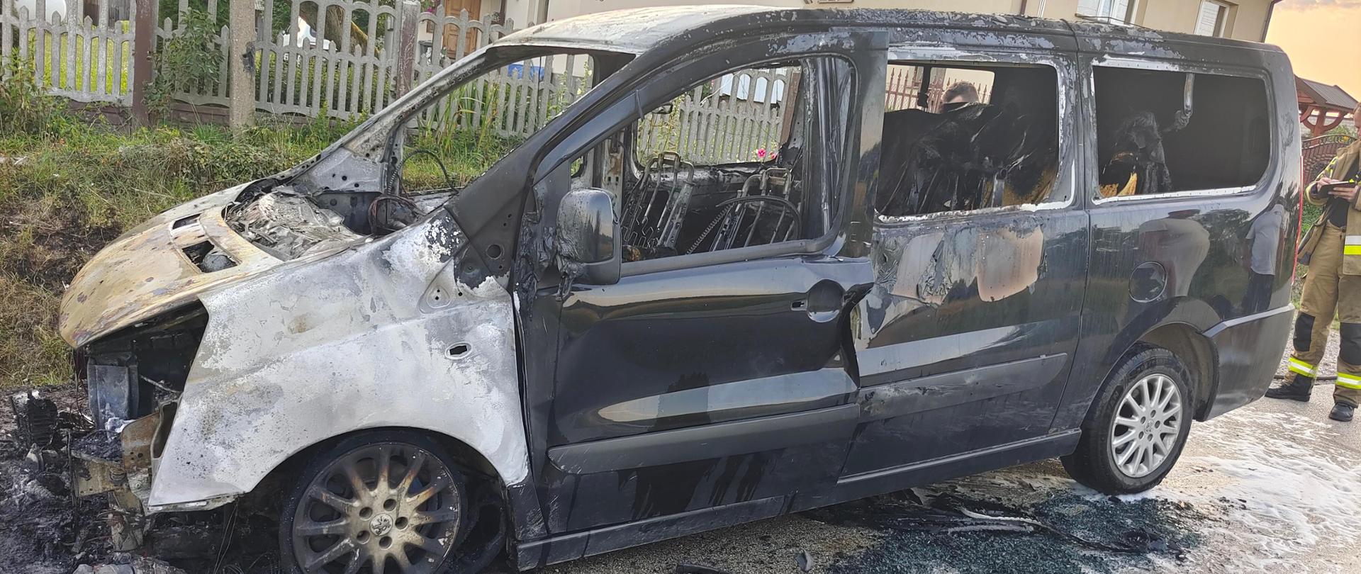 Zdjęcie przedstawia spalony samochód dostawczy stojący na poboczu drogi.