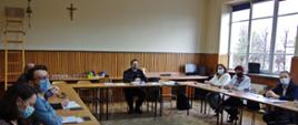 Widok z przodu. Na sali szkoleniowej przy stolikach siedzą uczestnicy spotkania. W centralnej części widoczny zastępca komendanta powiatowego PSP.