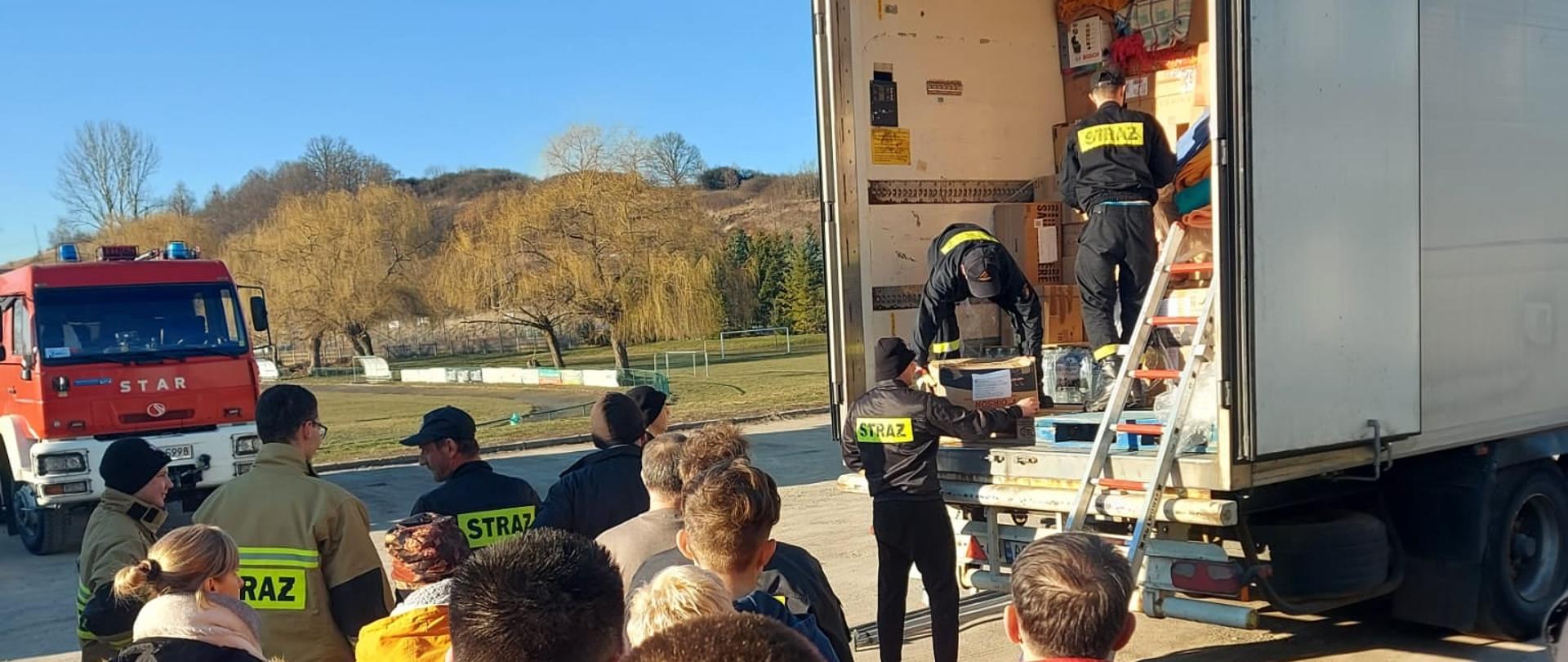 Zdjęcie przedstawia strażaków oraz osoby, które pomagają w rozładunku darów w ramach pomocy dla Ukrainy