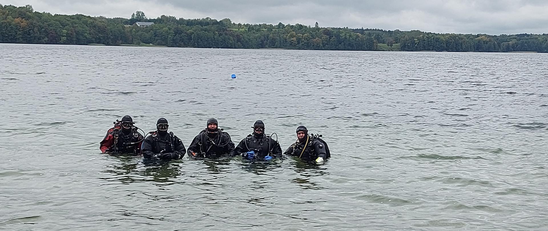 Nurkowie w pełnym akwalungu pozują w grupie w jeziorze.
