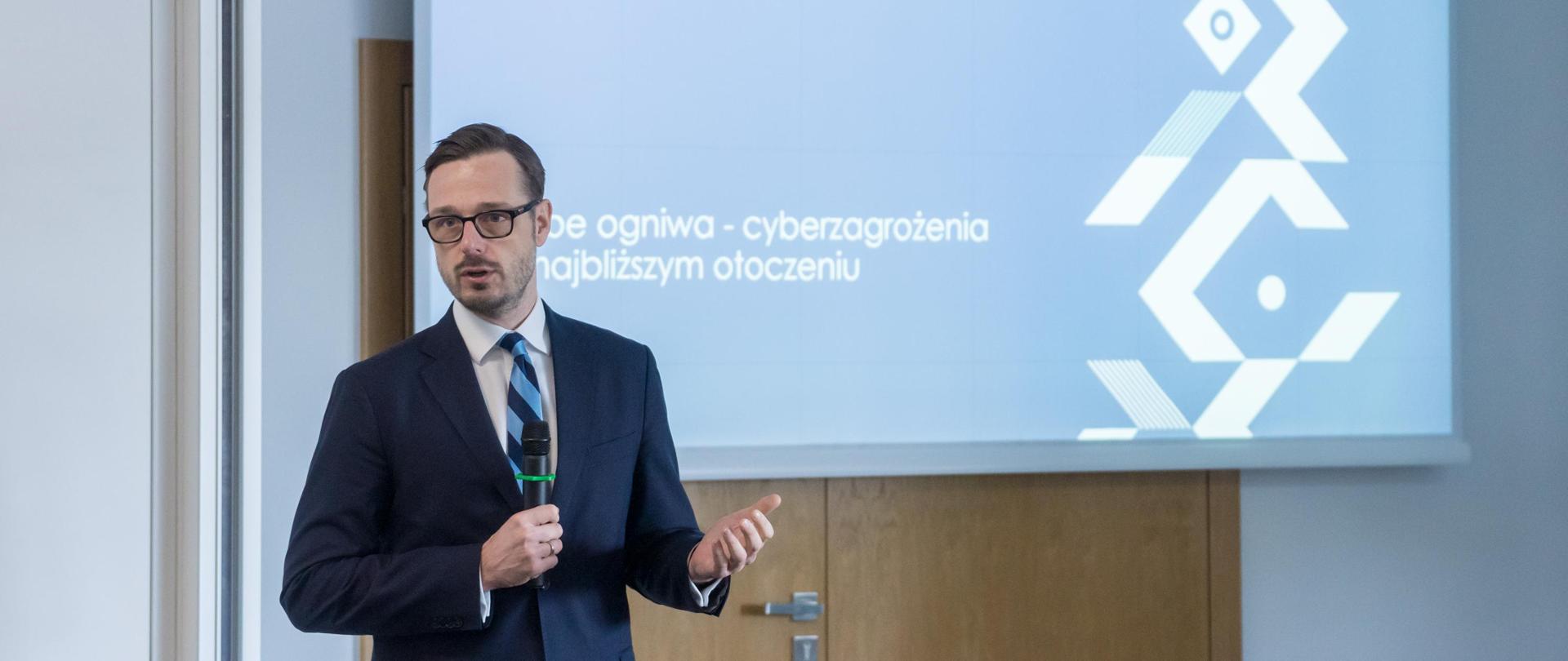 Minister Jakub Jaworowski przemawia przez mikrofon. W tle ekran z napisem NASK i tytułem szkolenia. 