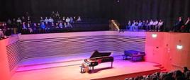 Wnętrze sali koncertowej wypełnione widzami. Na scenie pianistka grająca na fortepianie