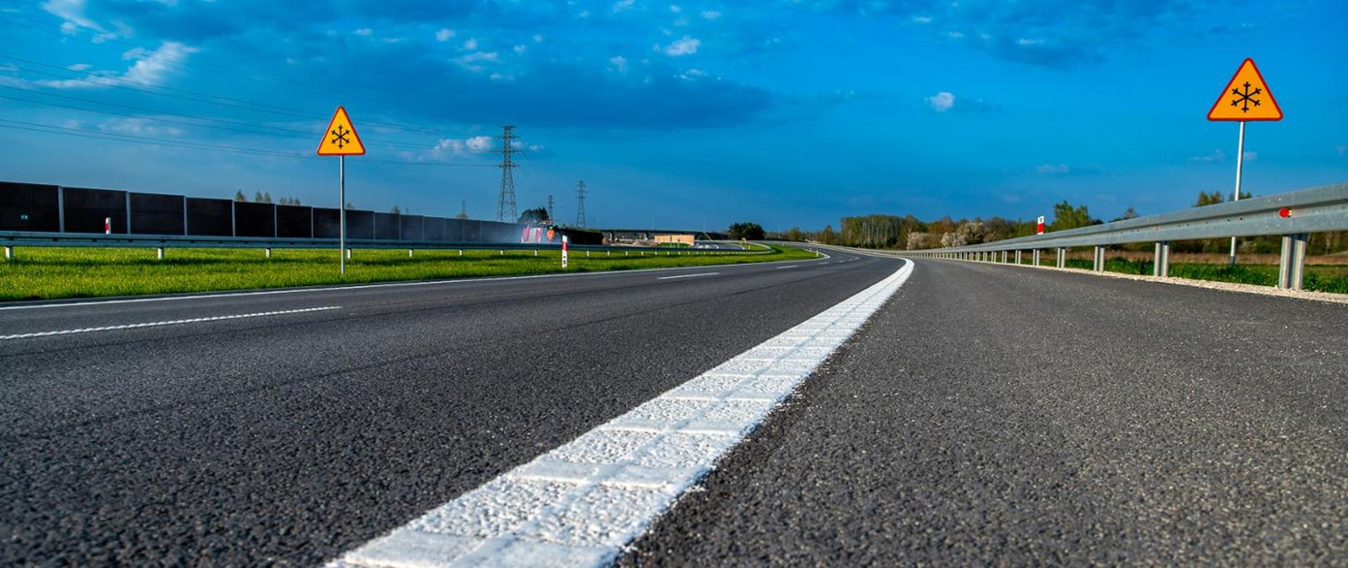 Zdjęcie drogi dwujezdniowej z pasem zieleni z dwoma pasami ruchu w każdym kierunku. Widoczne oznakowania pionowe.