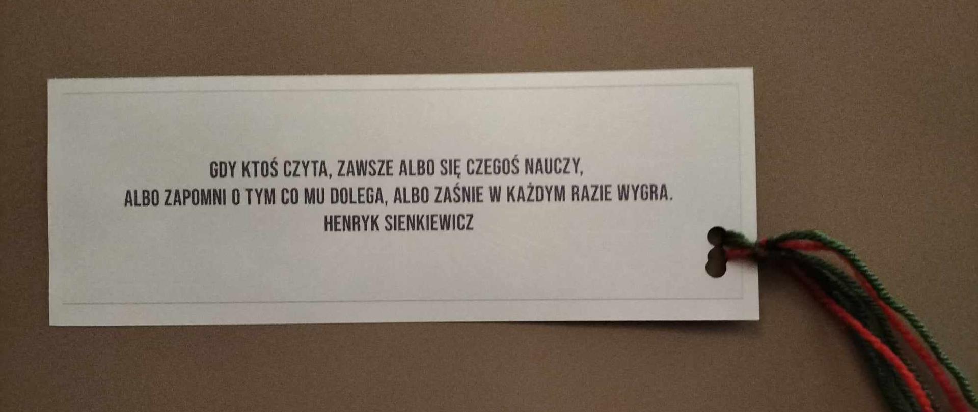 Na brązowym tle kartka z napisem: "gdy ktoś czyta, zawsze albo się czegoś nauczy, albo zapomni o tym co mu dolega, albo zaśnie w każdym razie wygra." Henryk Sienkiewicz