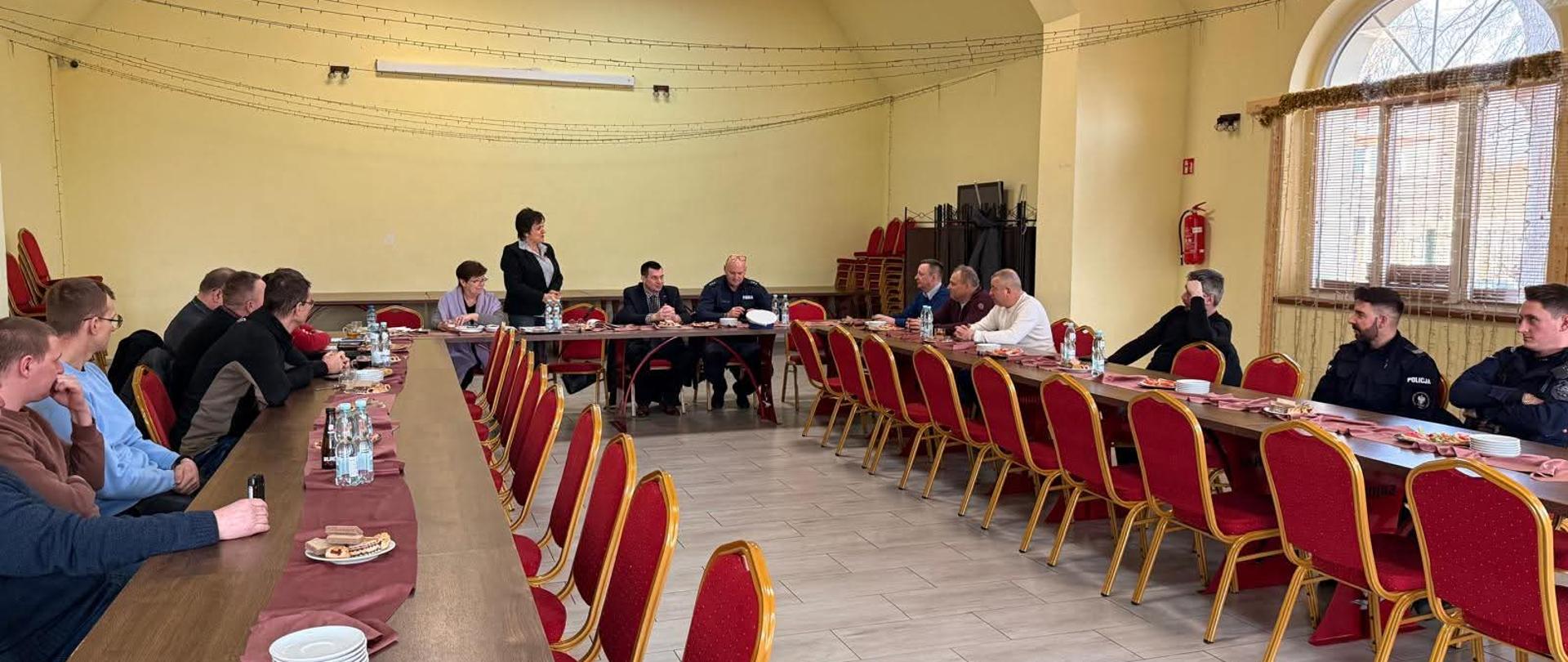 Zdjęcie przedstawia salę konferencyjną z układem stołów w formie litery U. Przy stołach siedzą rolnicy oraz policjanci.