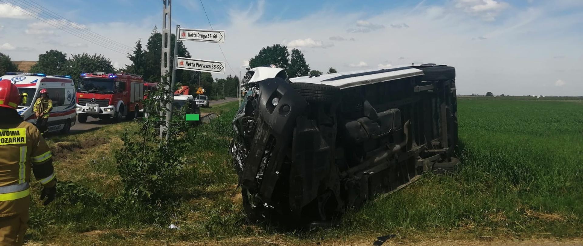 Na zdjęciu widać przewrócony samochód typu bus. W tle widać słuzby ratownicze.