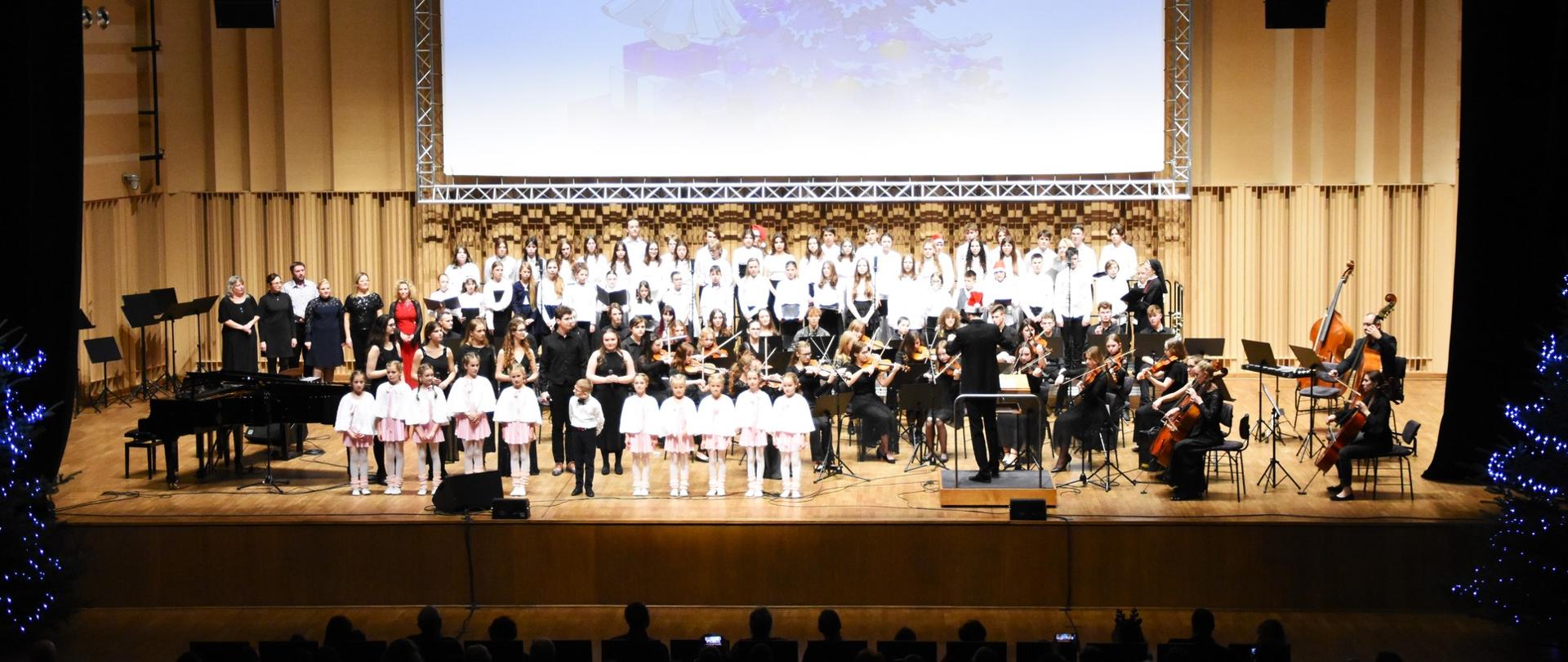 Scena Filharmonii Gorzowskiej - wykonawcy koncertu "Z kolędą przez świat"
Dzieci w różowo-białych strojach, wokaliści, orkiestra, chóry