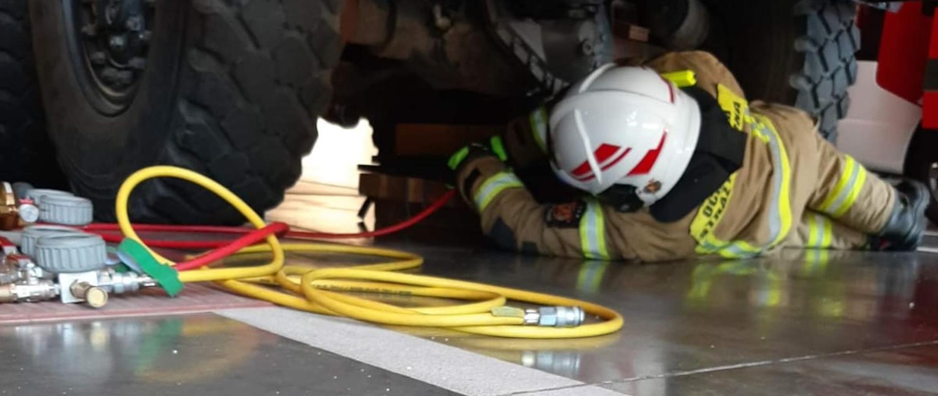 Strażak umieszcza poduszkę pneumatyczną niskiego ciśnienia na konstrukcji z klocków drewnianych pod samochodem w celu jego podniesienia. 