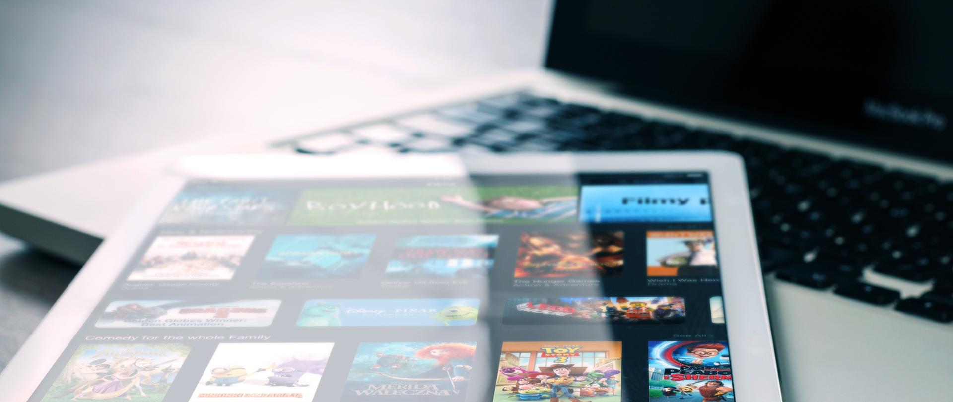 Zdjęcie w poziomie. Biały tablet leży na klawiaturze białego laptopa.