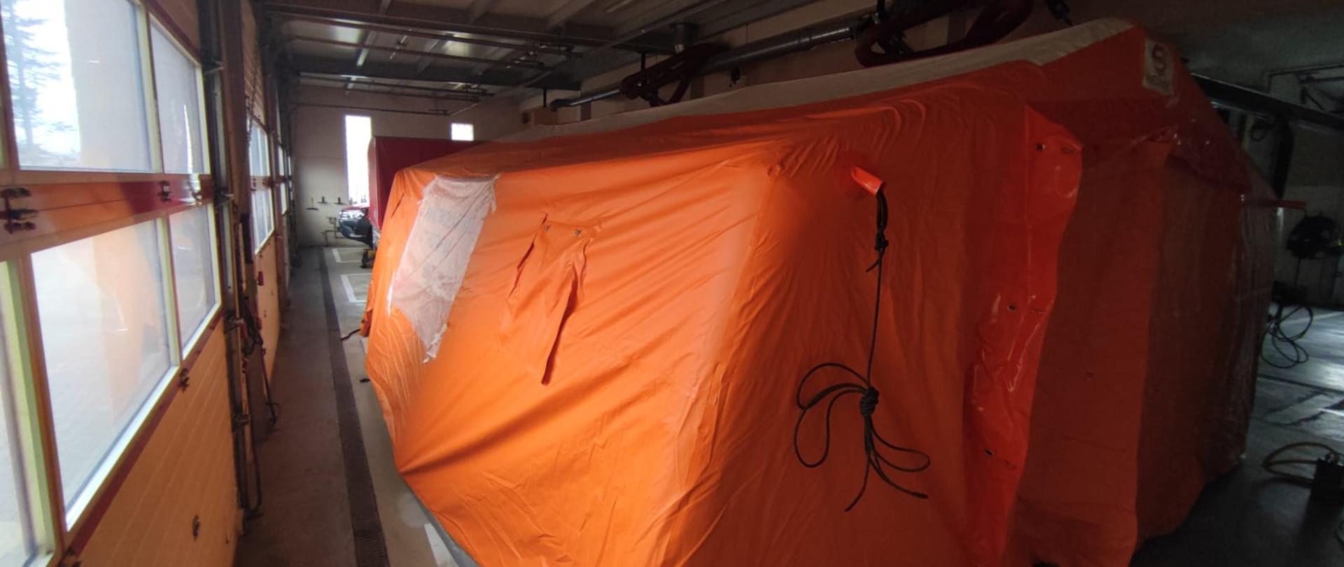 w pomieszczeniu garażowym stoi w pełni rozstawiony namiot pneumatyczny w kolorze pomarańczowym