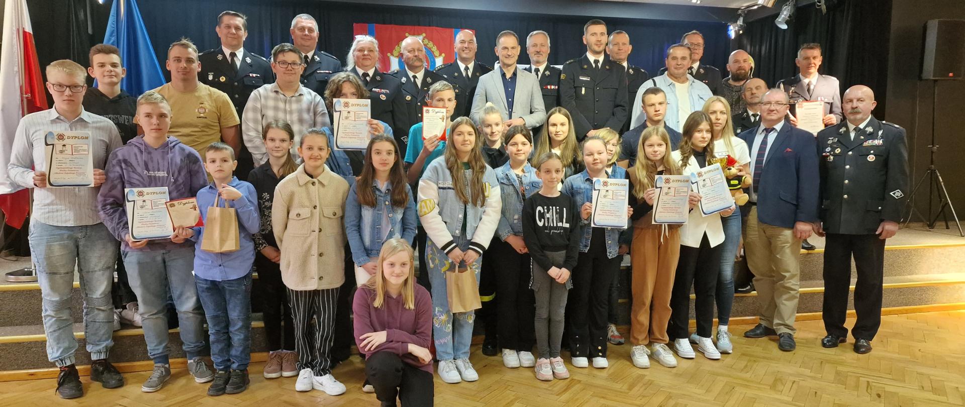 Zdjęcie przedstawia strażaków oraz druhów OSP i dzieci, które brały udział w Ogólnopolskim Turnieju Wiedzy Pożarniczej. 