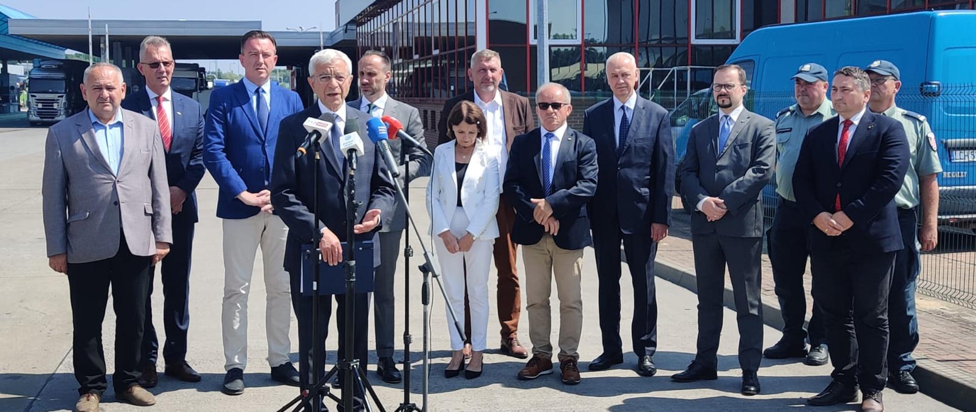 Uczestnicy konferencji prasowej stoją przed terminalem odpraw na przejściu granicznym.