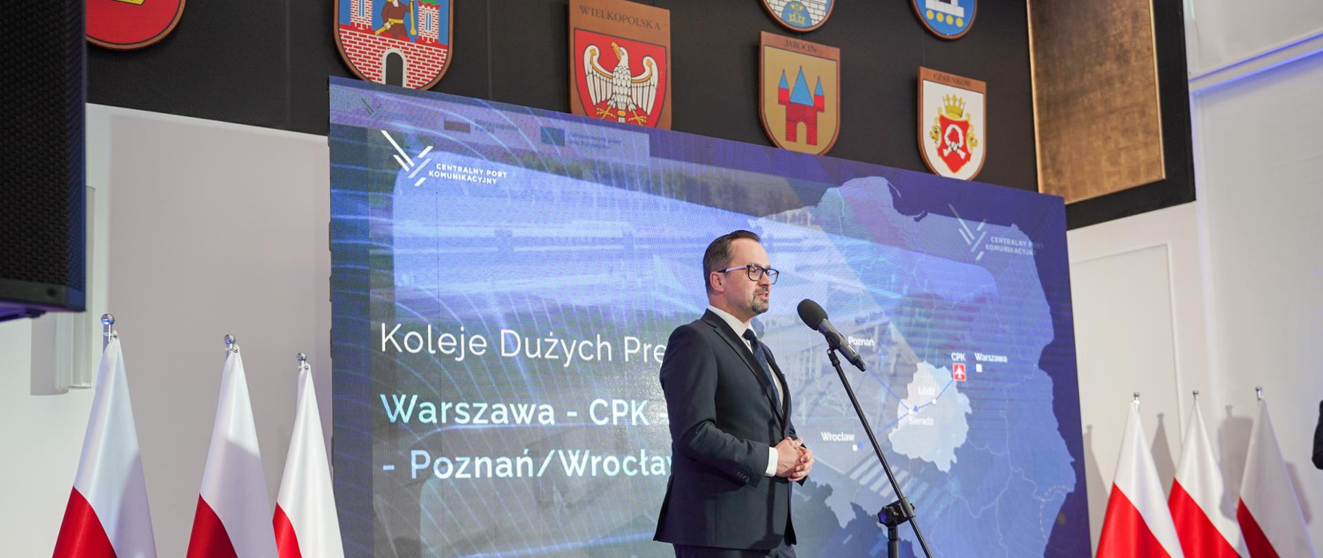 Wiceminister Marcin Horała stoi na scenie i mówi do mikrofonu.