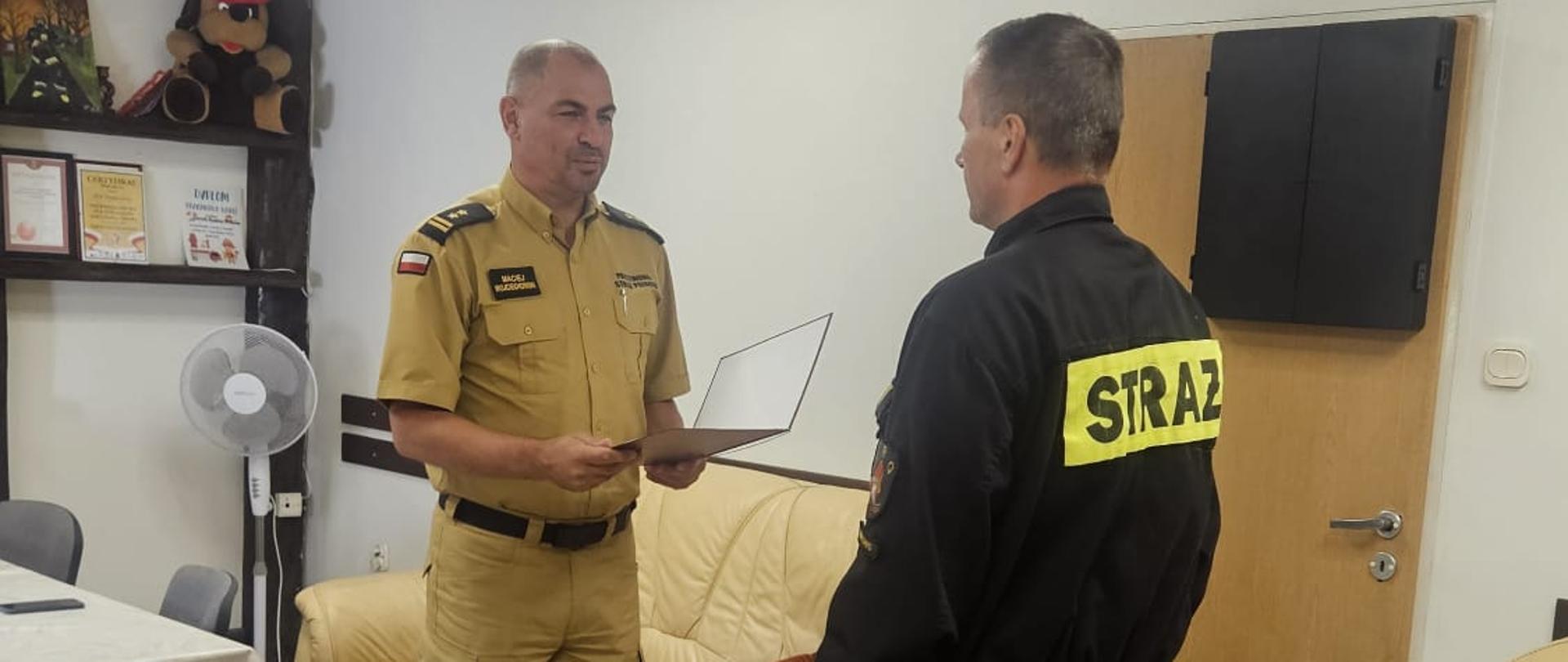 Spotkanie służbowe funkcjonariuszy PSP, podczas którego przekazywany jest dokument.