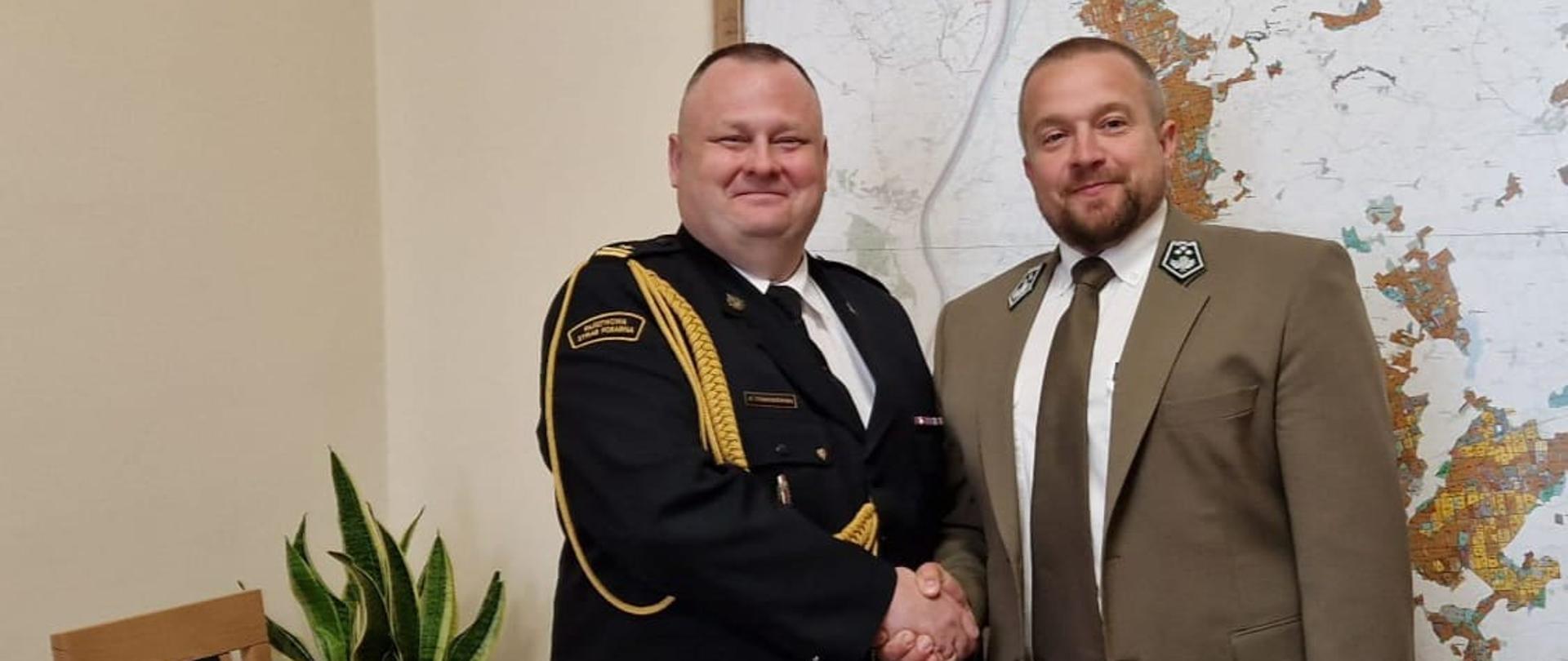 Komendant Straży Pożarnej i Nadleśniczy ściskają sobie ręce na tle mapy.