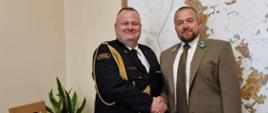 Komendant Straży Pożarnej i Nadleśniczy ściskają sobie ręce na tle mapy.