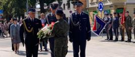 Rocznica wybuchu II WŚ Zdjęcie przedstawia plac przed pomnikiem Żołnierza Polskiego. Na pierwszym planie znajduje się delegacja służb mundurowych: Państwowej Straży Pożarnej, Służby Więziennej i Policji. Funkcjonariusze występują w umundurowaniu galowym. Przed nimi uczennica klasy mundurowej , która odbiera wiązankę kwiatów. Z prawej strony stoją w szeregu poczty sztandarowe, z tyłu natomiast pozostałe delegacje.