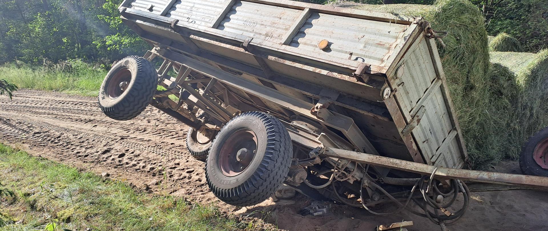 Na zdjęciu widać przechyloną przyczepę oraz bele siana, które z niej spadły.