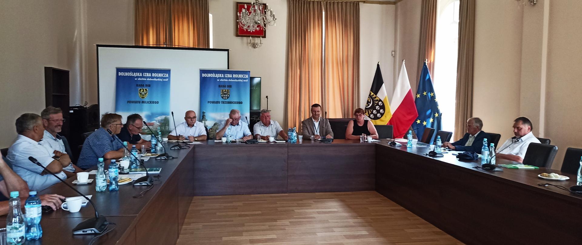 Uczestnicy posiedzenia siedzą przy stołach ustawionych w podkowę w sali konferencyjnej. W tle widoczne są banery Dolnośląskiej Izby Rolniczej oraz flagi: Dolnego Śląska, Polski i Unii Europejskiej.