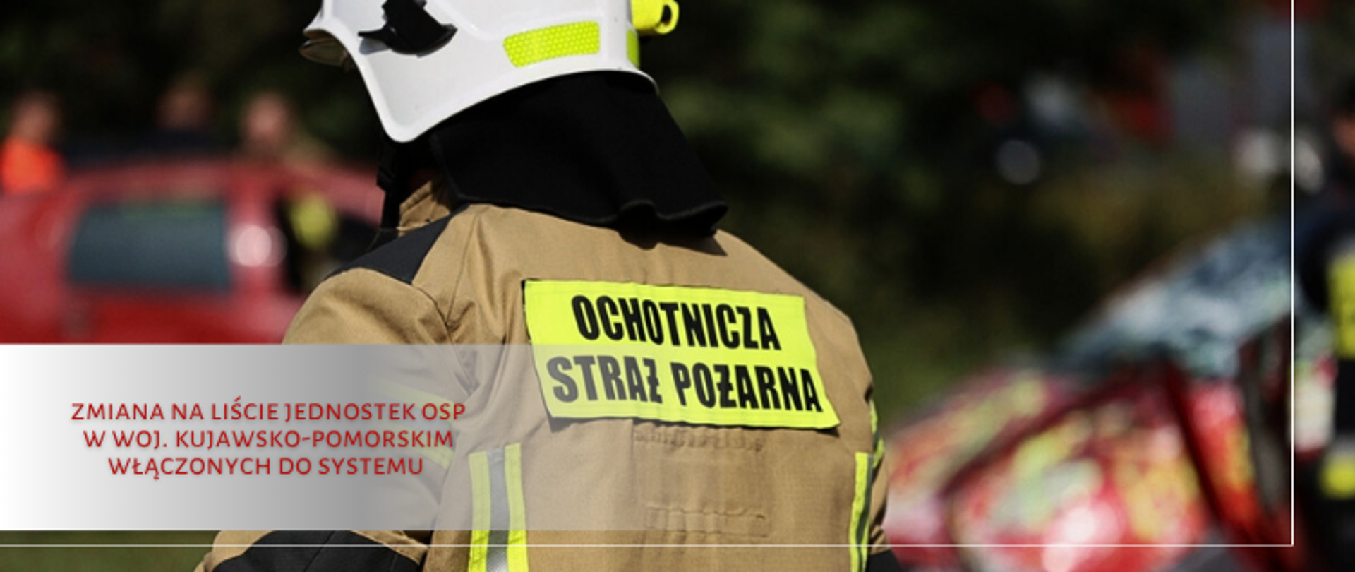 Strażak odwrócony tyłem, na głowie biały hełm, na plecach napis Ochotnicza Straż Pożarna.