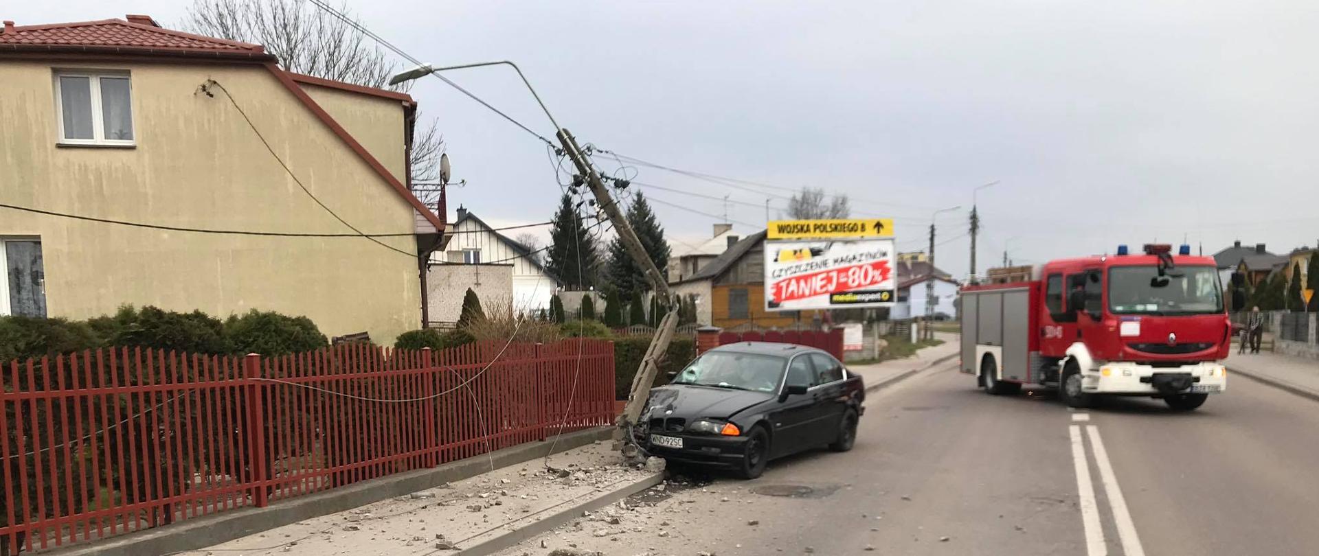 samochód osobowy stojący na pasie jezdni po uderzeniu w słup elektryczny, w tle samochód ratowniczo-gaśniczy