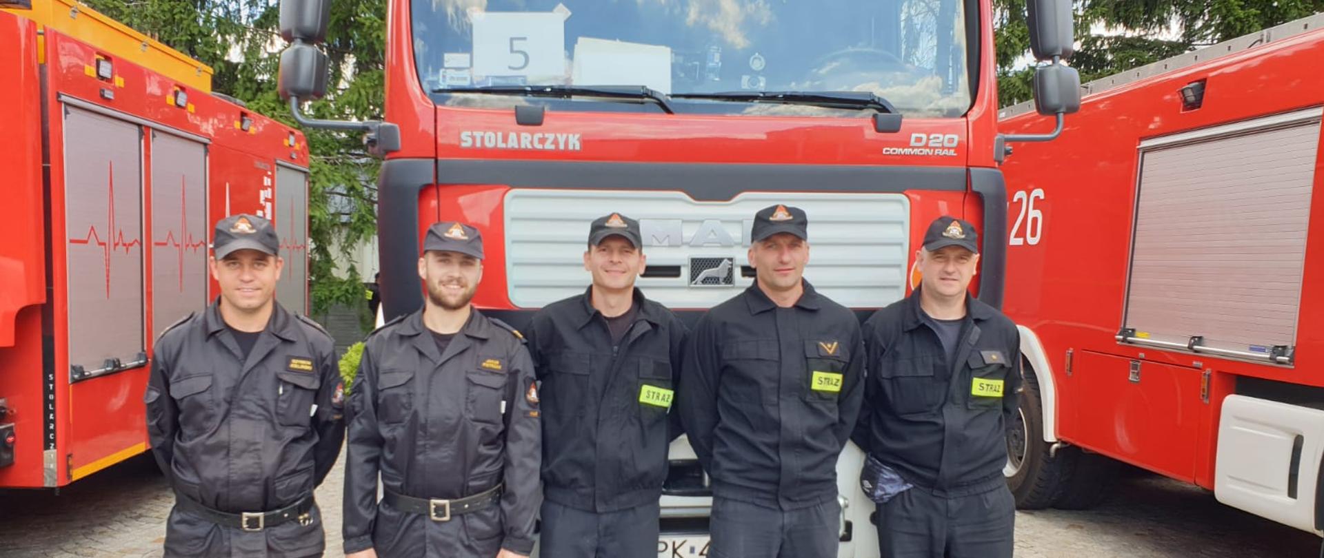 Na zdjęciu widać funkcjonariuszy Komendy Miejskiej Państwowej Kaliszu na tle samochodu ratowniczo-gaśniczego. Funkcjonariusze (pięć osób) ubrani w umundurowanie koszarowe i dowódczo-sztabowe.