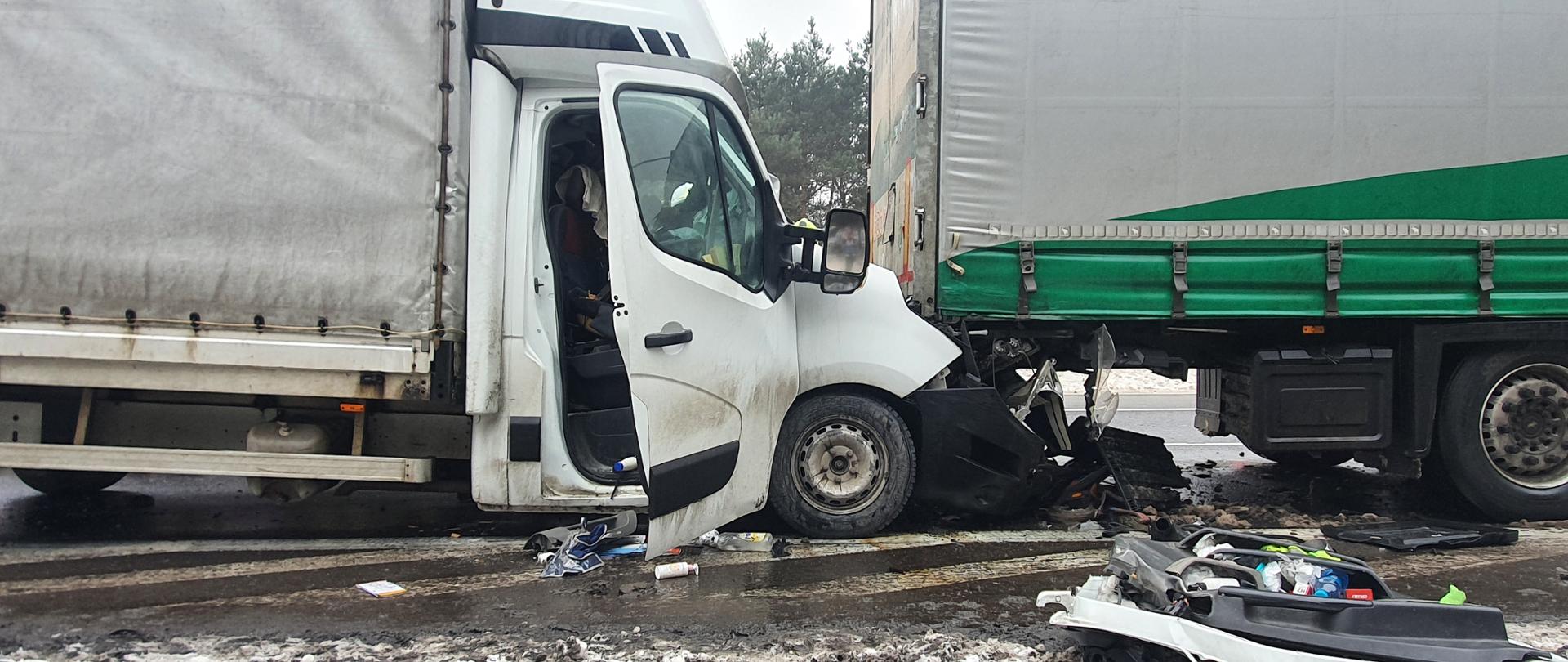 Po lewej stronie zdjęcia zniszczony samochód dostawczy koloru białego po prawej stronie naczepa ciężarowa