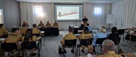 strażacy i inne osoby siedzą w sali konferencyjnej, na ekranie rzutnika wyświetlony jest slajd o treści Państwowa Straż pożarna biuro kadr
