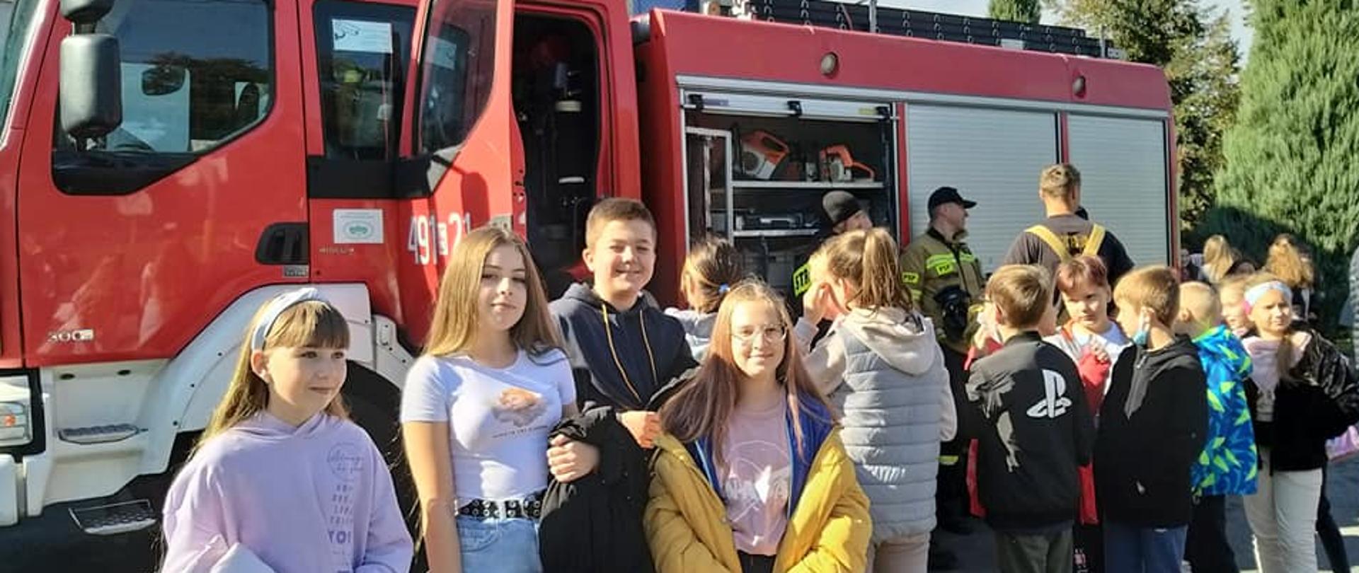 Zdjęcie przedstawia zapoznanie uczniów ze sprzętem na średnim samochodzie pożarniczym