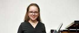 Dziewczynka na tle fortepianu w ręku trzyma dyplom i figurkę bociana