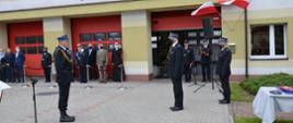 Zdjęcie przedstawia złożenie meldunku przez dowódcę uroczystości Zastępcy Komendanta Wojewódzkiego na tle budynku KP PSP w Wieluniu podczas uroczystości Dnia Strażaka, widoczni także zaproszeniu goście i Komendant Powiatowy