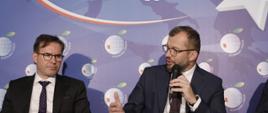 Minister funduszy i polityki regionalnej Grzegorz Puda przemawia podczas panelu dyskusyjnego na Forum w Karpaczu. Obok (po lewej stronie) siedzi mężczyzna.