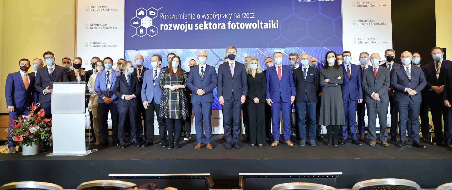 Podpisanie Porozumienia o współpracy na rzecz rozwoju sektora fotowoltaiki z udziałem wiceministra Włodzimierza Bernackiego, uczestnicy uroczystości podpisania porozumienia stoją razem na scenie.