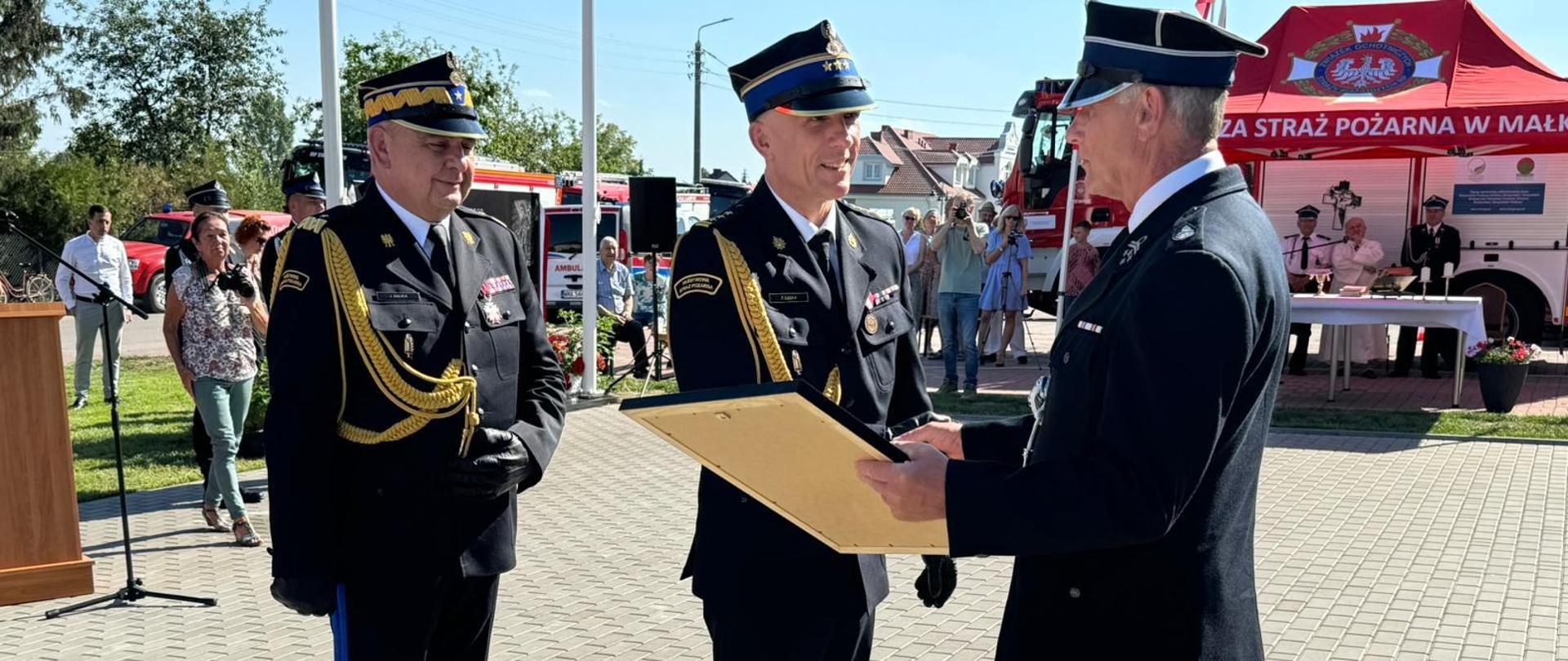 Zastępca Mazowieckiego Komendanta Wojewódzkiego PSP wręcza obraz Prezesowi OSP. Obok niego stoi Zastępca Komendanta Głównego PSP.