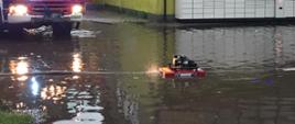 Zdjęcie przedstawia zalaną ulicę Wyspiańskiego w Szczytnie, w trakcie działań straży pożarnej po przejściu nawałnicy. Strażacy wypompowują wodę z zalanej ulicy.