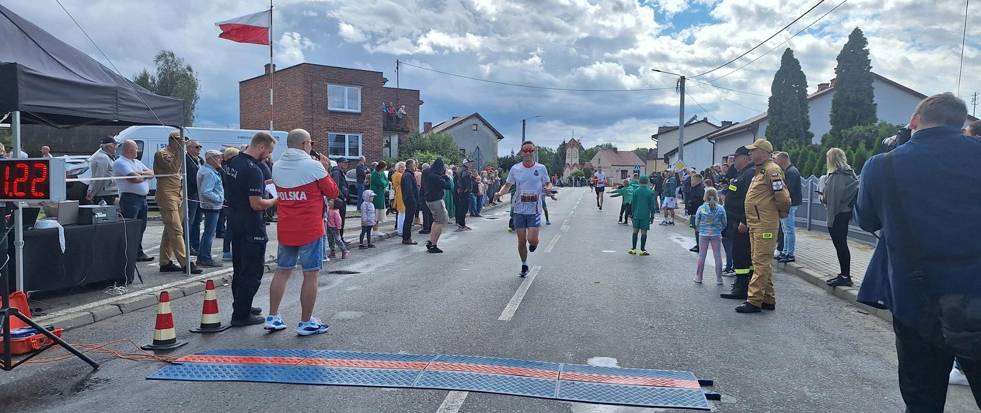 zawodnik biegnie ulicą, na poboczach stoją kibice