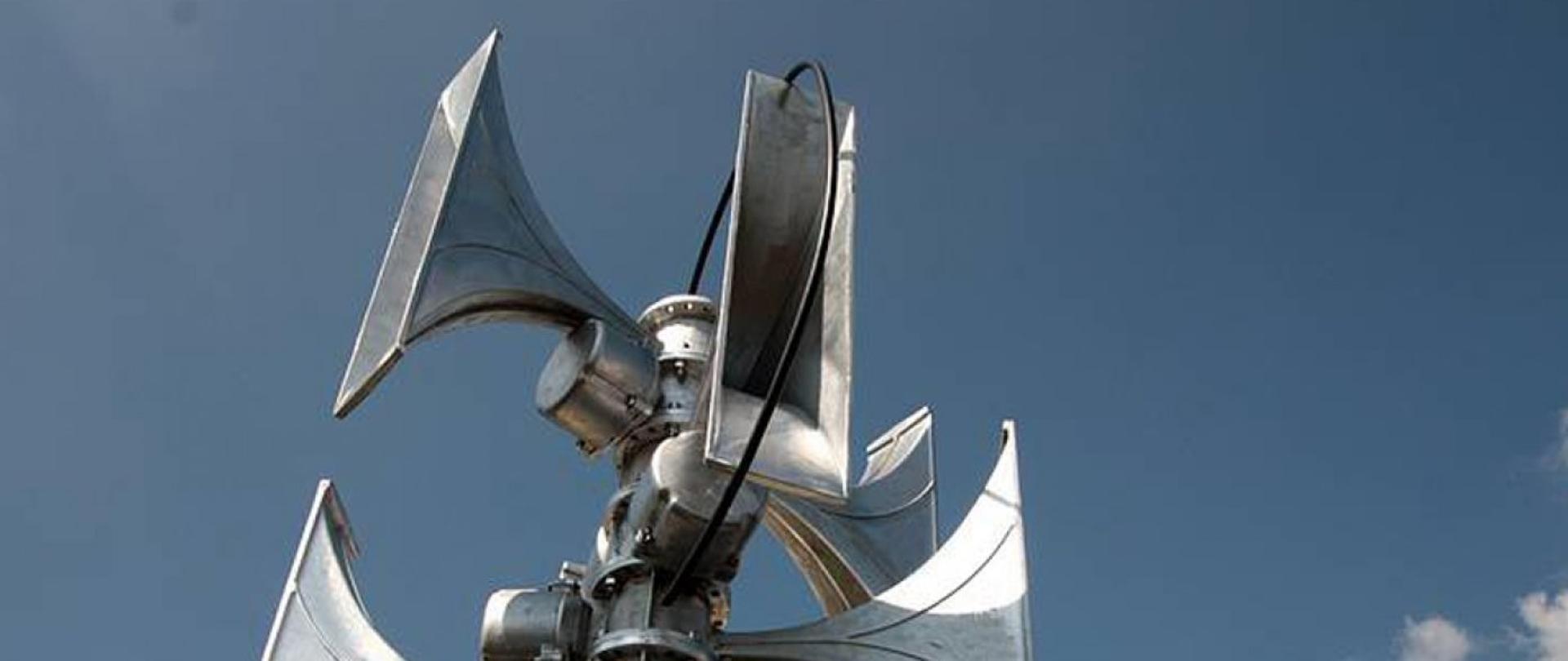 Zdjęcie przedstawia część elementów systemu ostrzegania i alarmowania, tj. głośniki szczelinowe umieszczone na maszcie.