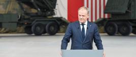 Premier Donald Tusk podczas przemówienia w jednostce wojskowej w Sochaczewie. W tle flagi Polski i USA oraz sprzęt wojskowy.