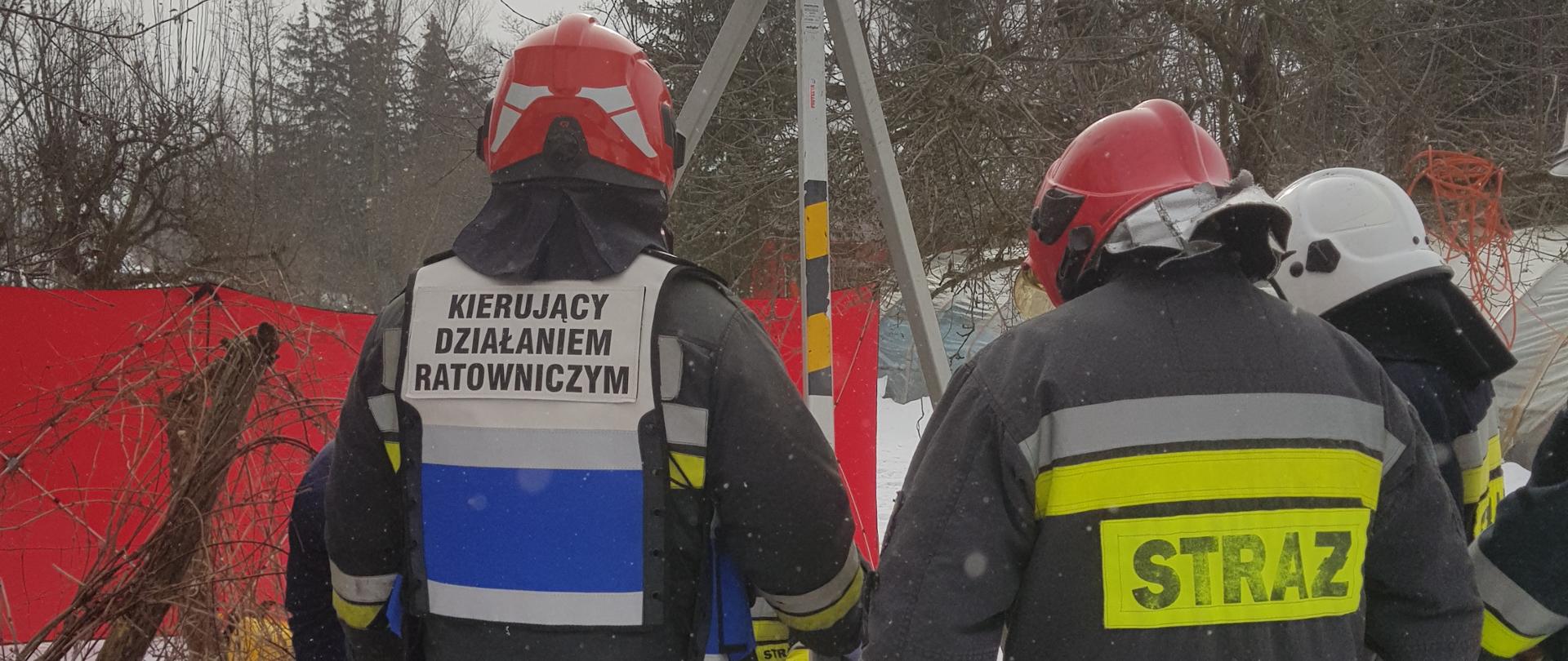 Grupa strażaków rozstawia trójnóg ratowniczy, który wykorzystany będzie do zejścia do studni.